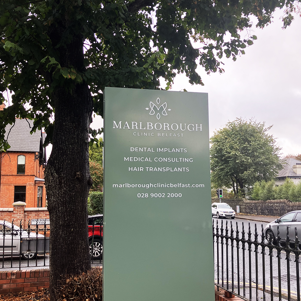 Green monolith sign with practice logo, services and contact details at Marlborough Clinic Belfast
