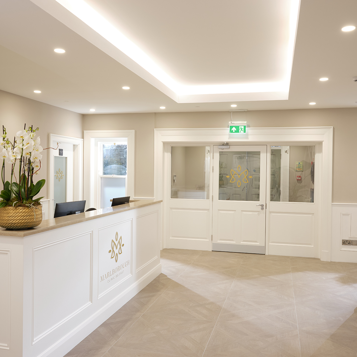 Reception area featuring gold practice logos on reception desk and door glass at Marlborough Clinic Belfast